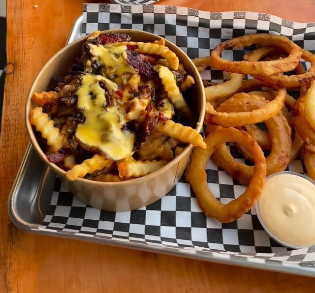 Onion rings and a cup of loaded crinkle fries on a checkered-paper tray