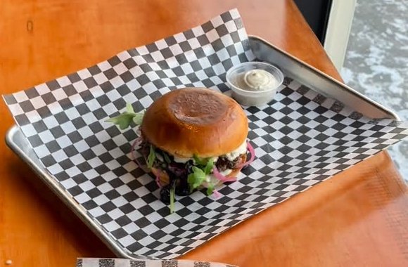 Truffle Berry burger with arugula and pickled onion on a steel tray by the window
